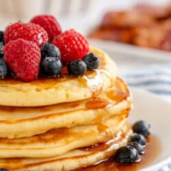 A stack of pancakes topped with fresh berries and maple syrup on a white plate.