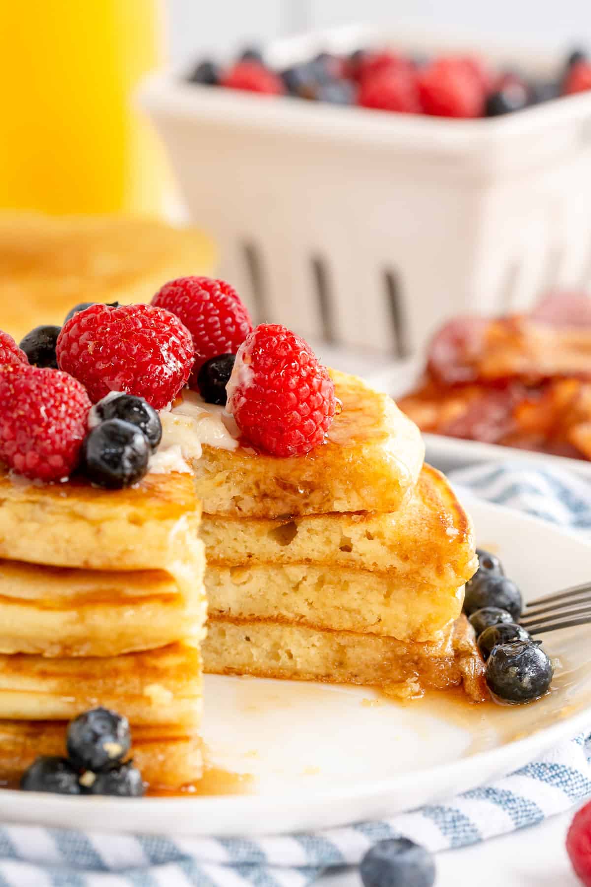 A stack of pancakes topped with berries and maple syrup with a section cut out.