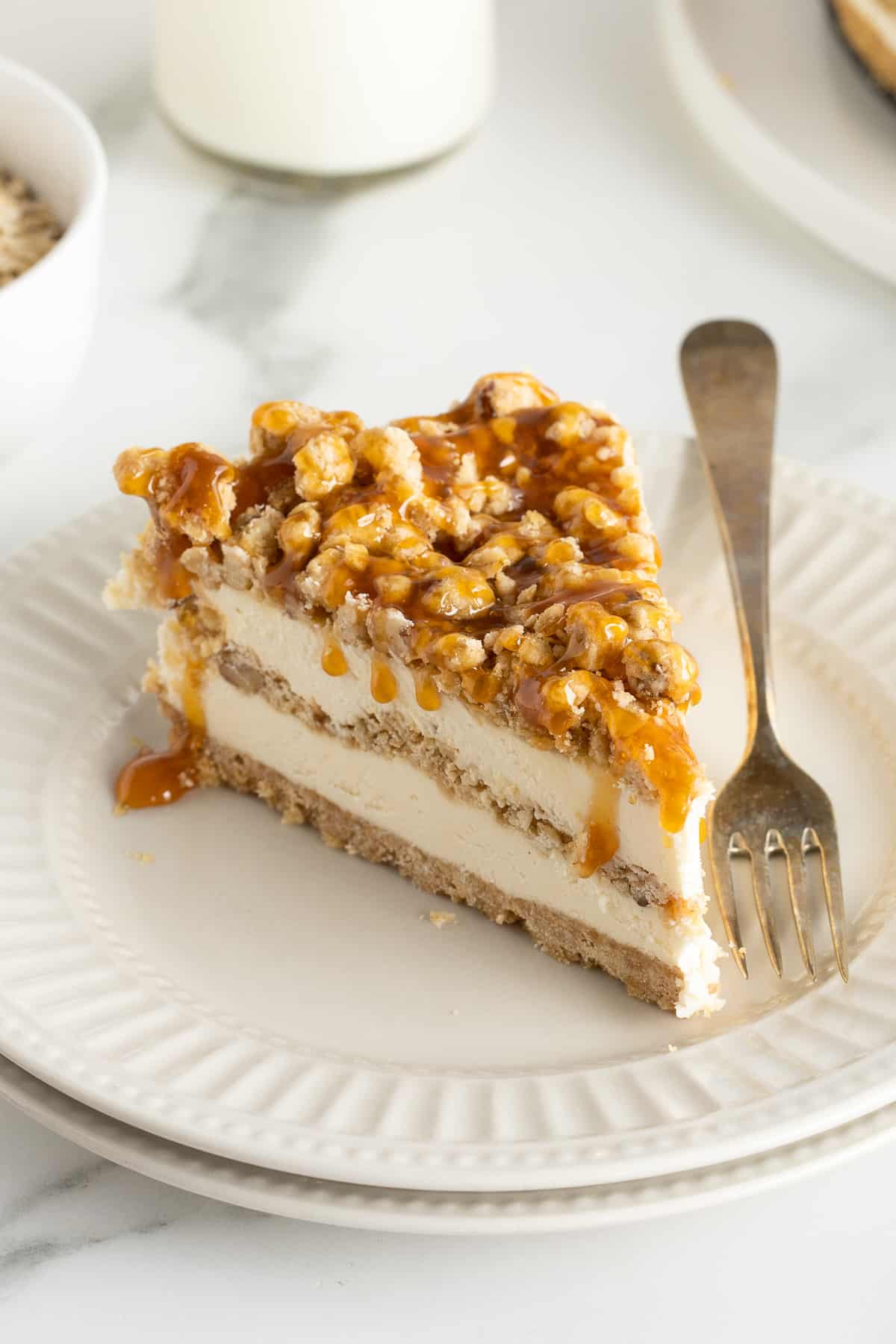 A slice of frozen dessert with ice cream topping drizzled over the top on a white plate with a fork.