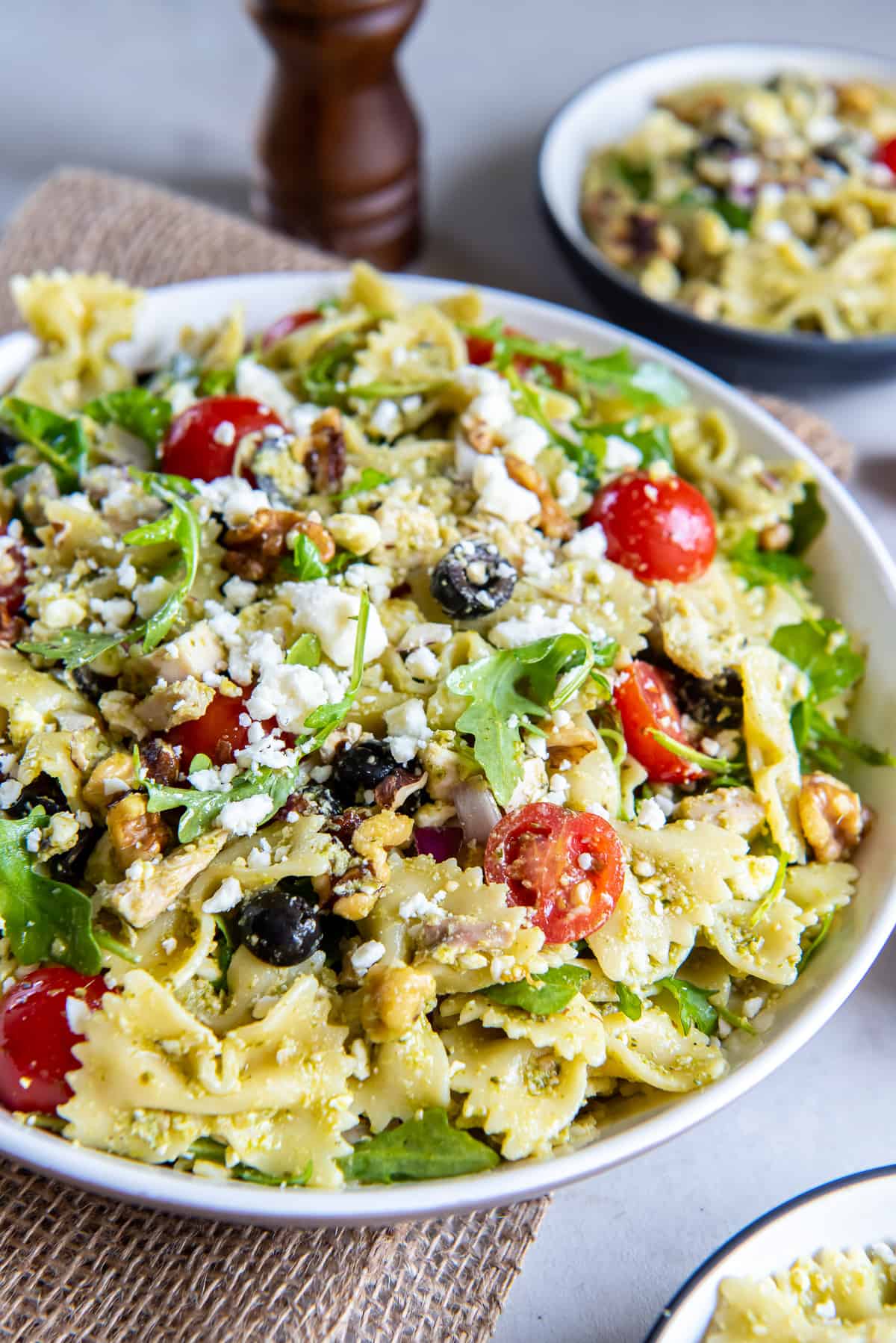 A side view of a large serving bowl filled with chicken pesto pasta salad.