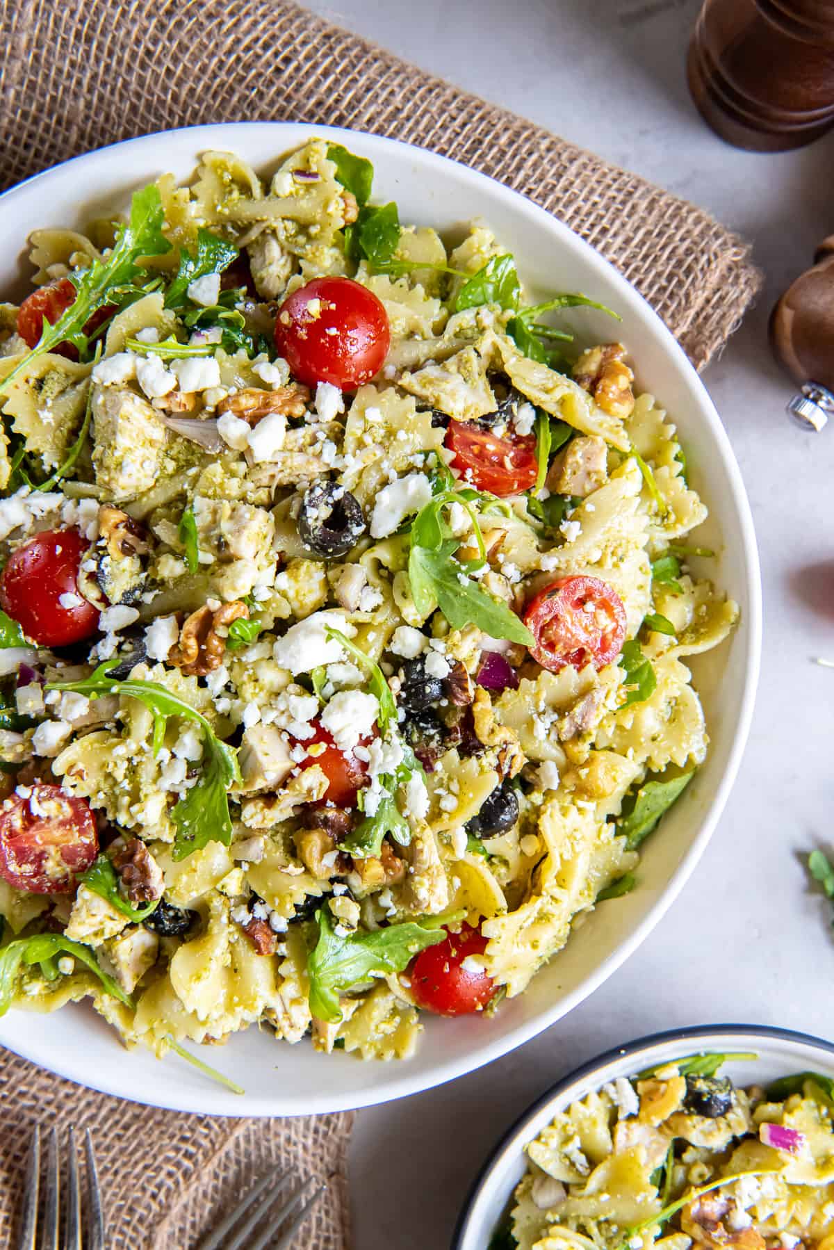 A top down shot of a large serving bowl filled with pasta salad with chicken, pesto, cherry tomatoes, and feta cheese.