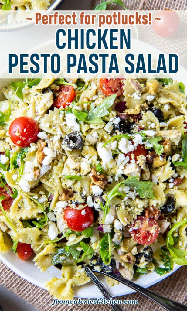 A top down shot of serving spoons resting in a large serving bowl filled with chicken pesto pasta salad with text.