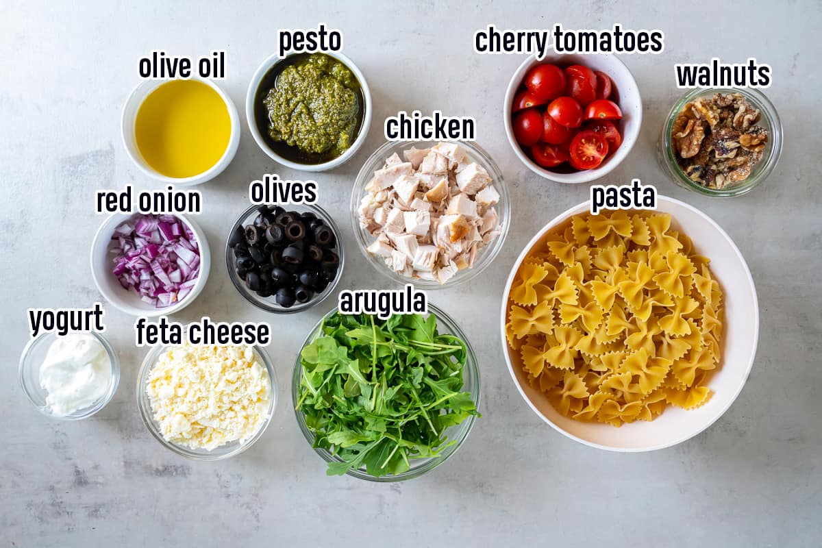 Cooked cubed chicken, bowtie pasta, pesto, and other ingredients in bowls with text.