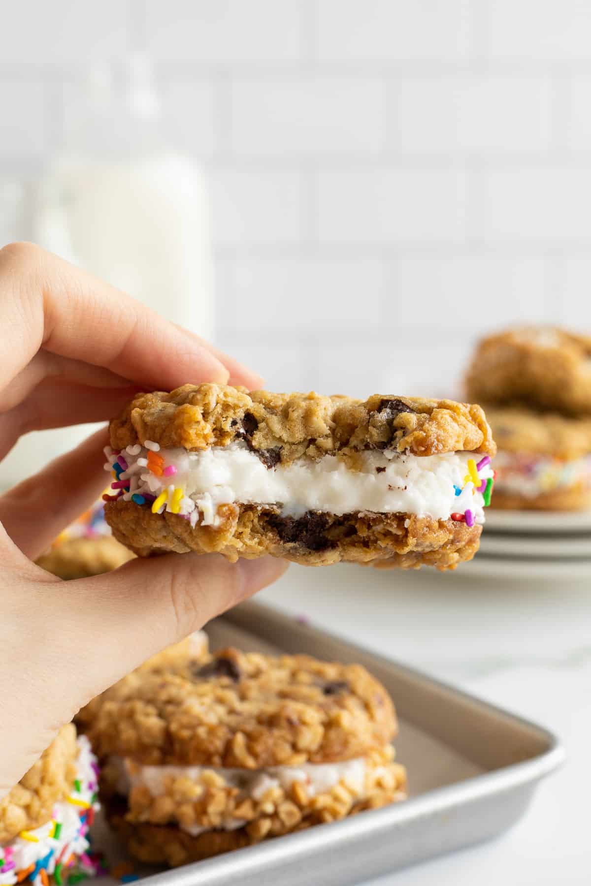 A hand holding a cookie ice cream sandwich with a bite missing.