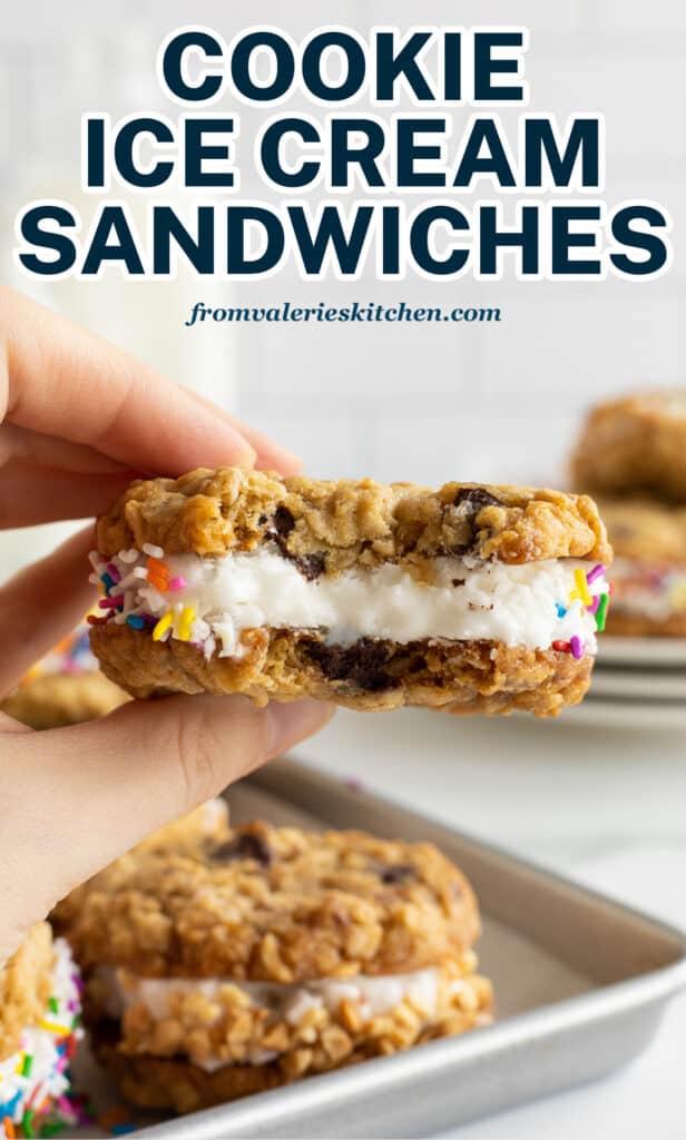 A hand holding a cookie ice cream sandwich with a bite missing.