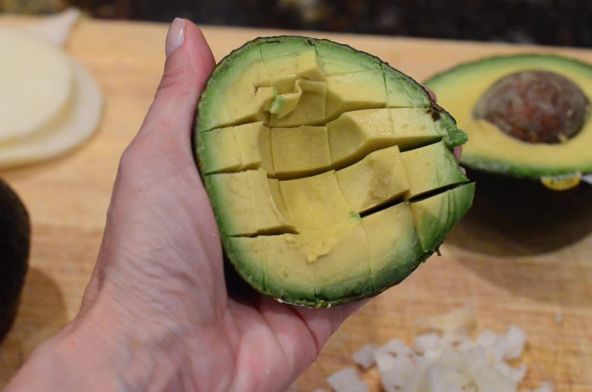 A hand holds a sliced avocado in its shell.