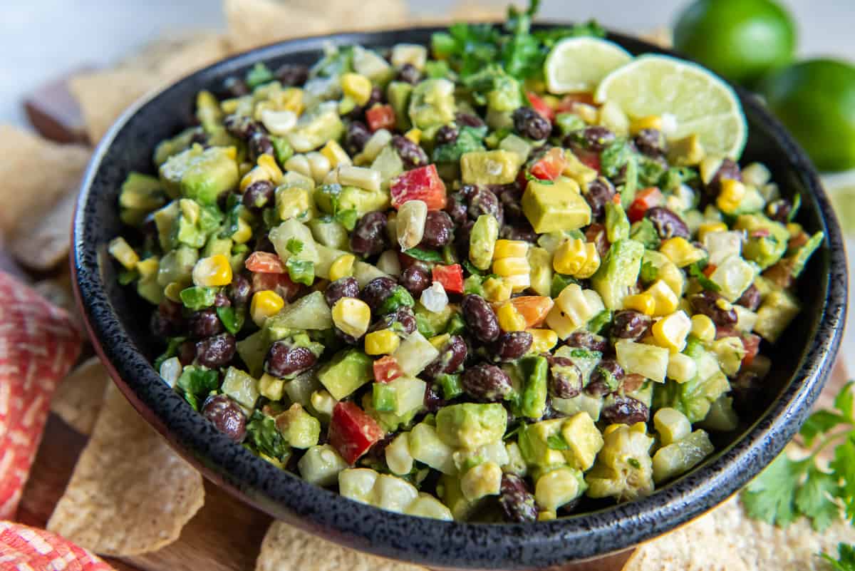 A black bowl filled with loaded guacamole with tortilla chips lying around it.