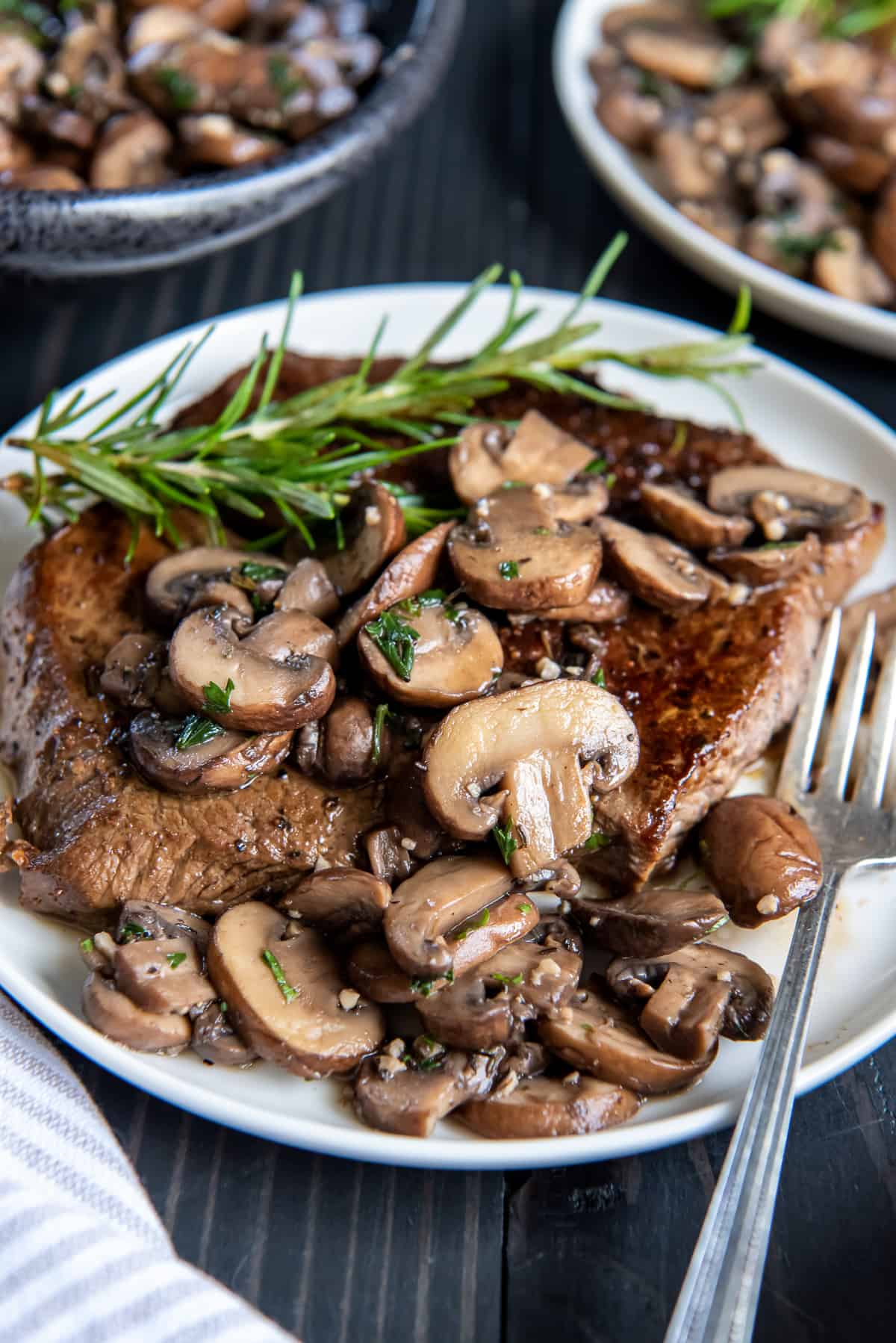 Cooked steak smothered with sauteed mushrooms on a white plate with a fork.