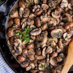 A top down shot of sauteed mushrooms in a cast iron skillet with a wooden spoon.