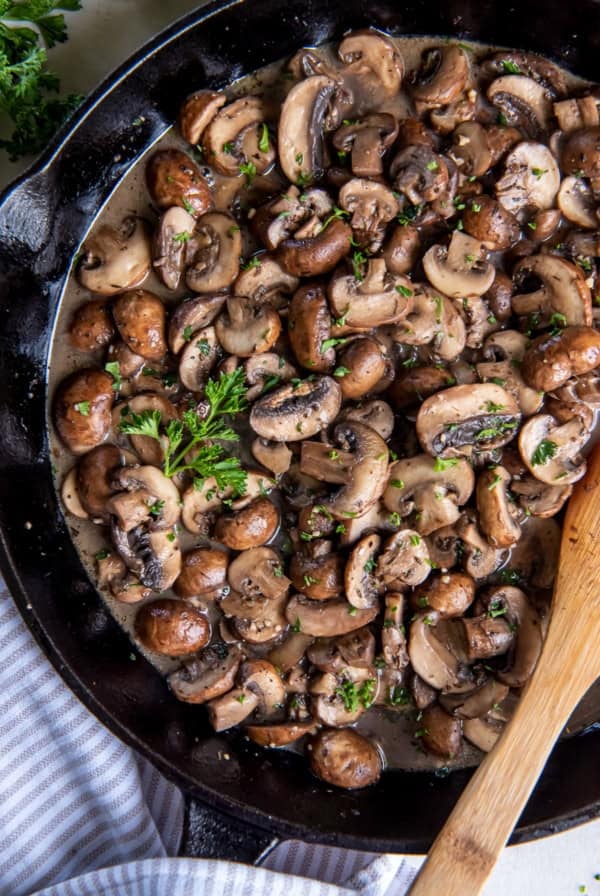 A top down shot of sauteed mushrooms in a cast iron skillet with a wooden spoon.