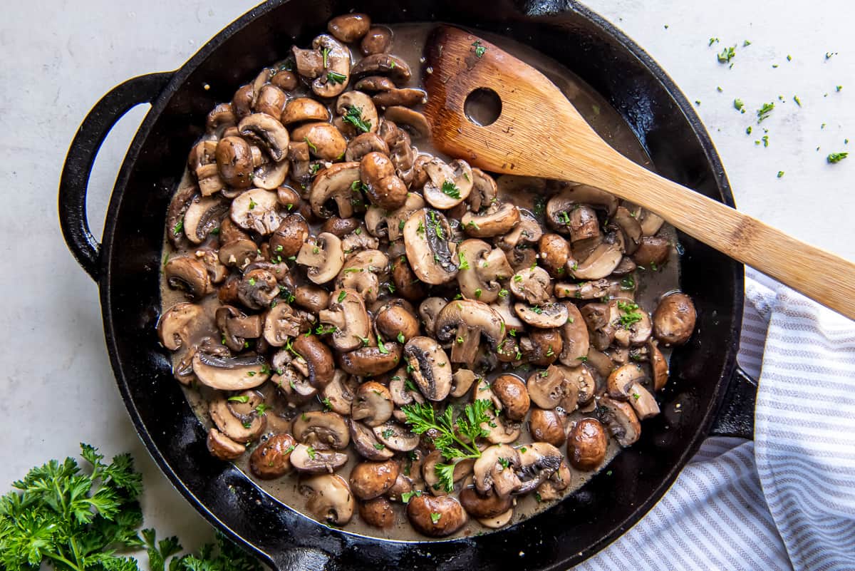 A top down shot of sauteed mushrooms in a cast iron skillet with a wooden spoon.