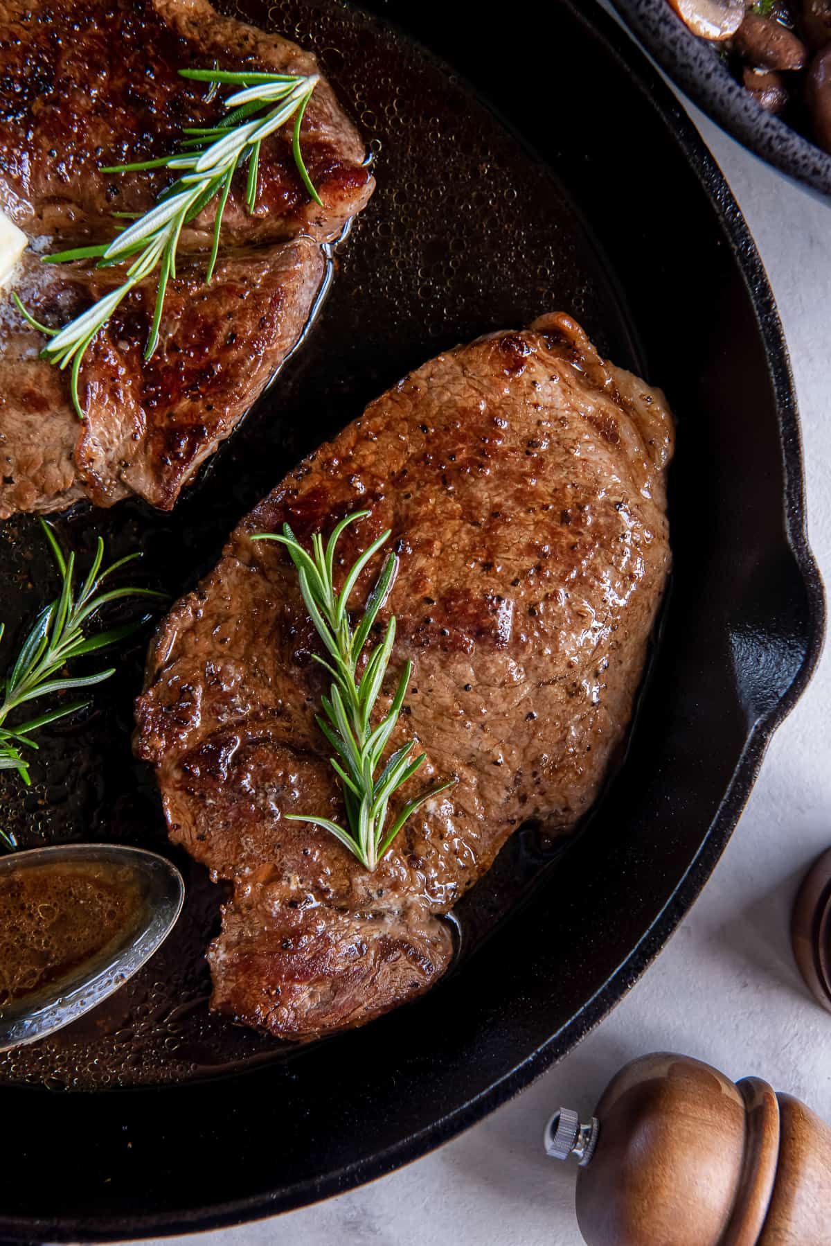 A top down shot of two steaks topped with sprigs of rosemary in a cast iron skillet.