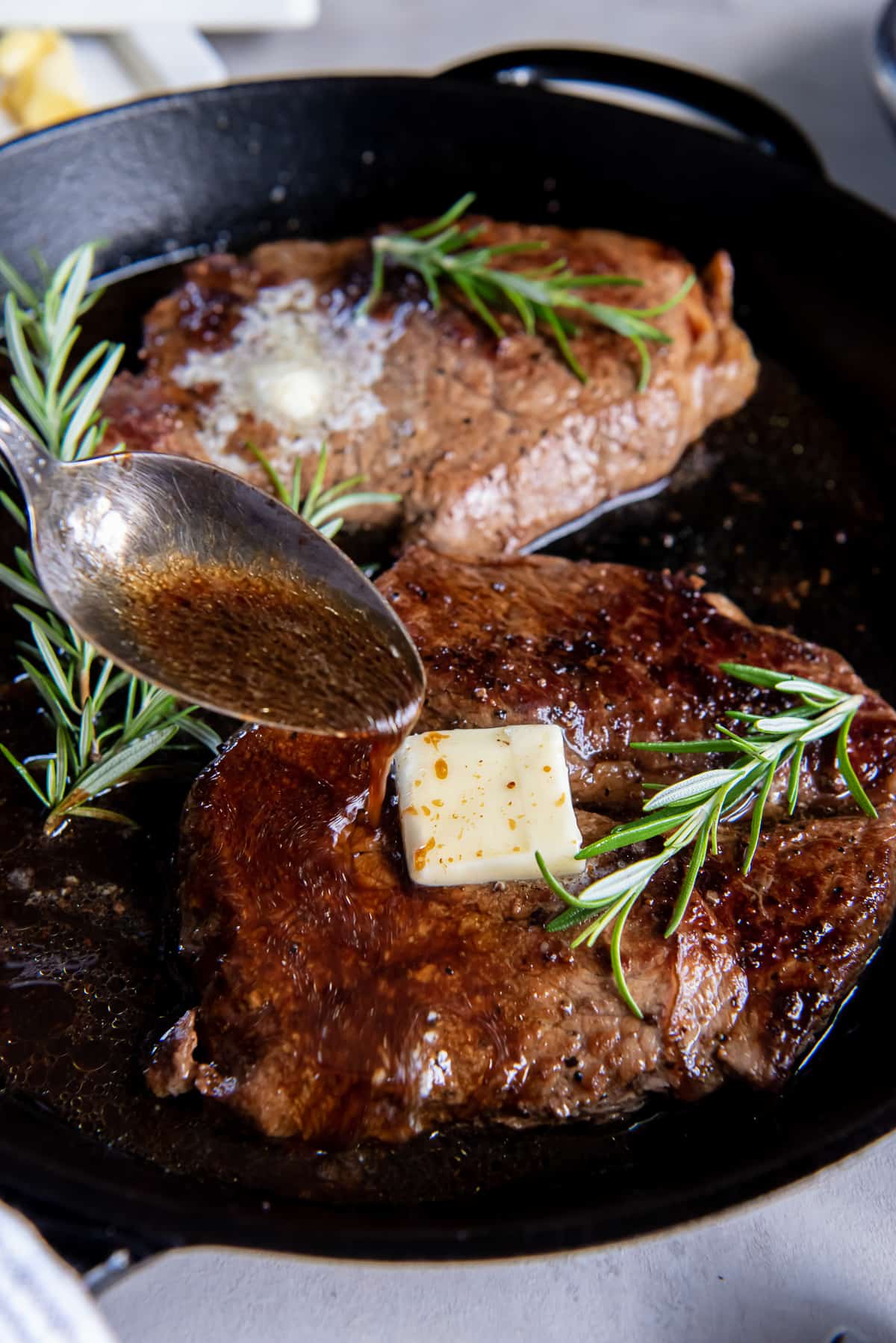 A spoon pouring pan juices over a sirloin steak in a cast iron skillet.