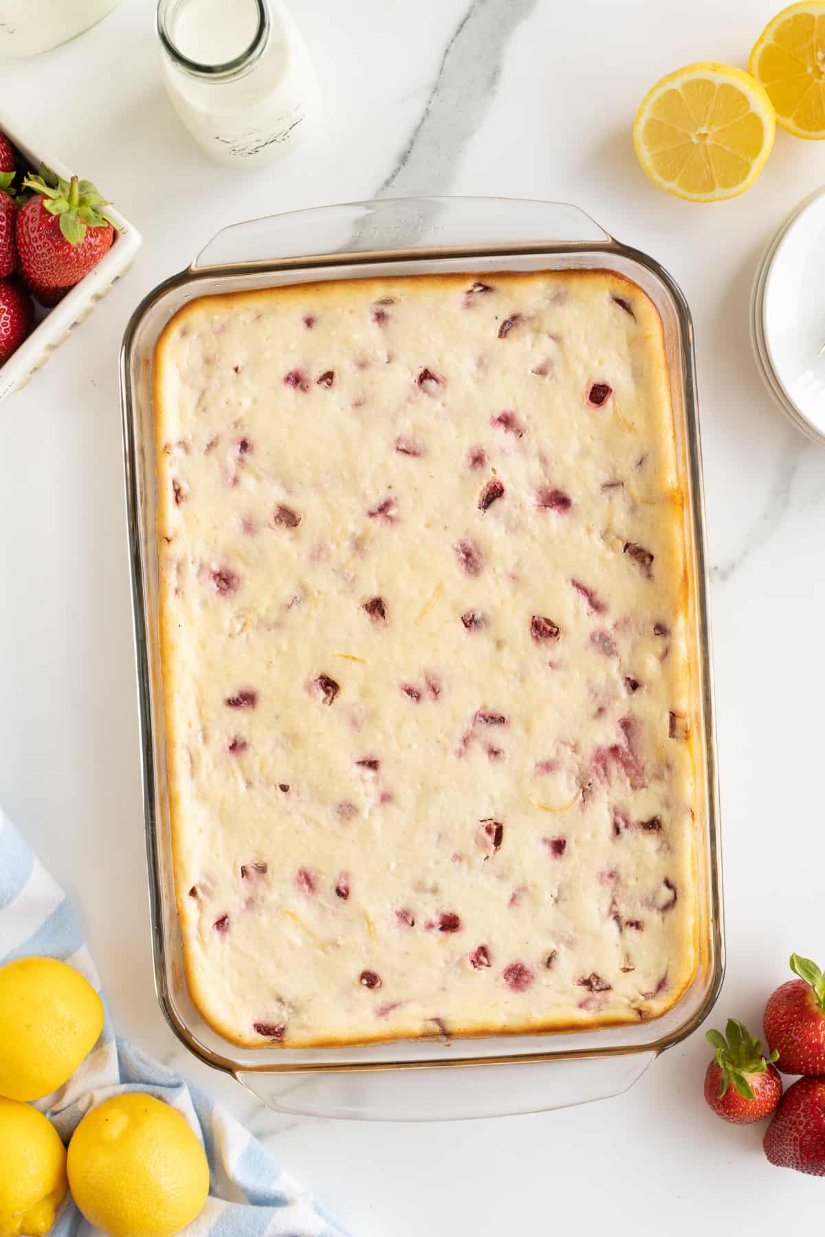 A top down shot of Strawberry Cheesecake Bars in a glass baking dish with lemons and strawberries set around it.