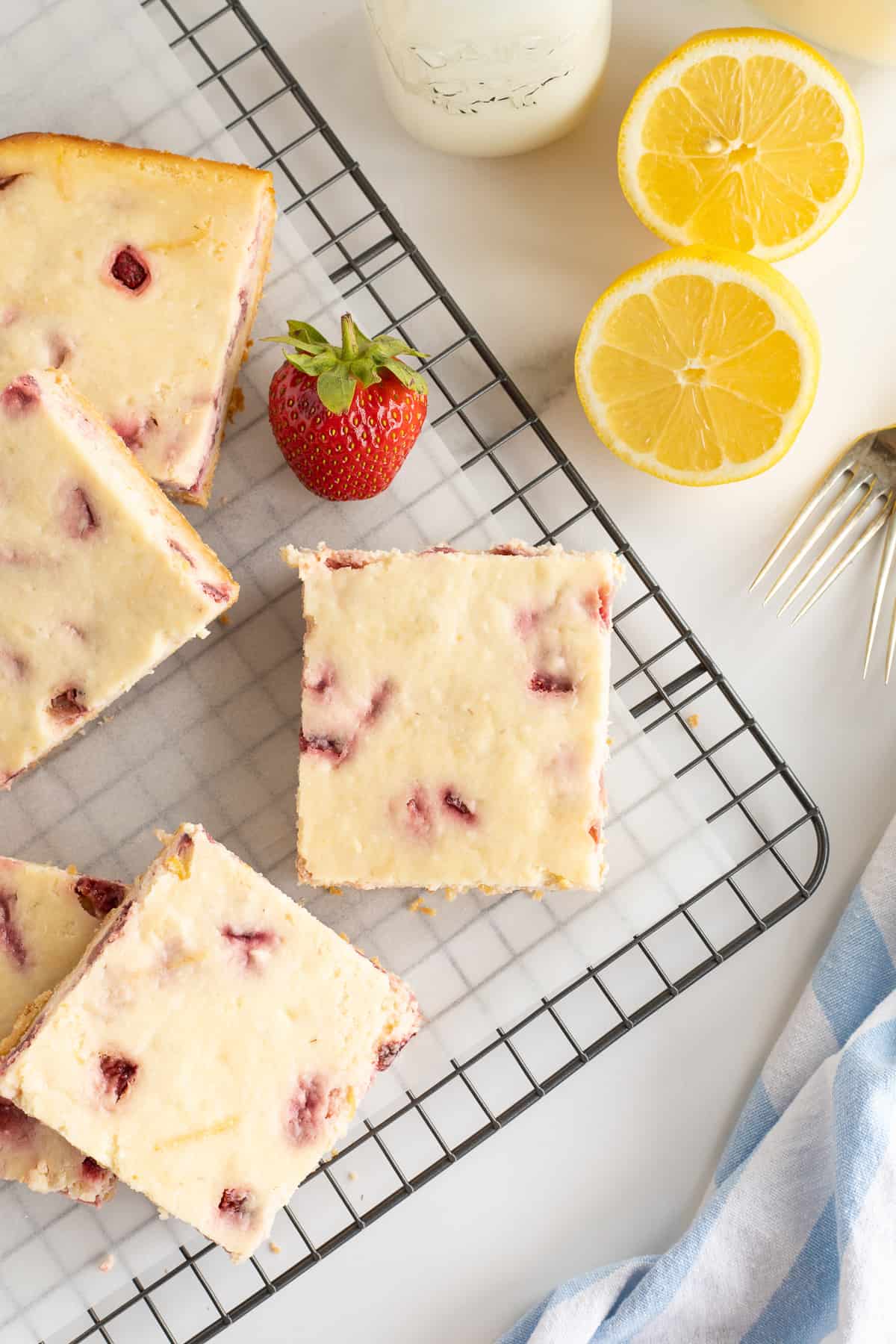 A top down shot of sliced Strawberry Cheesecake Bars on a wire rack next to a strawberry and lemon halves.