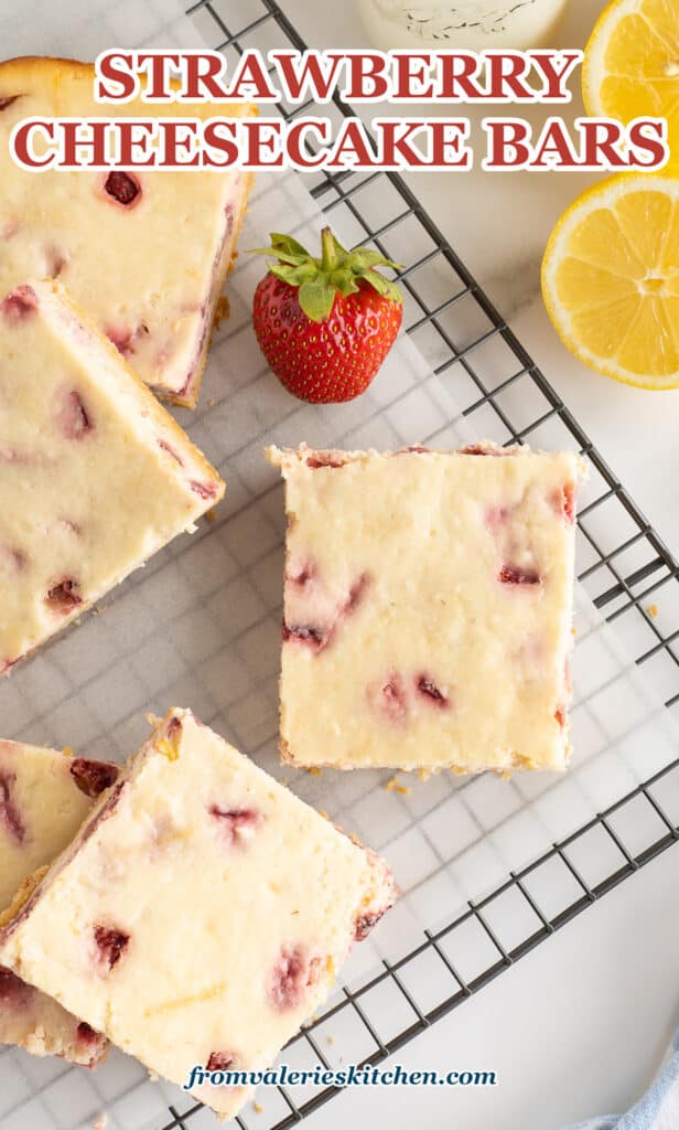 A top down shot of sliced Strawberry Cheesecake Bars on a wire rack next to a strawberry and lemon halves with text.