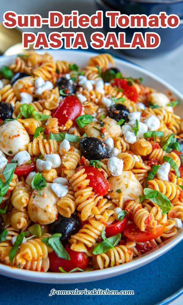 A side view of a large bowl filled with pasta salad with tomatoes, black olives, mozzarella balls, and basil with text.
