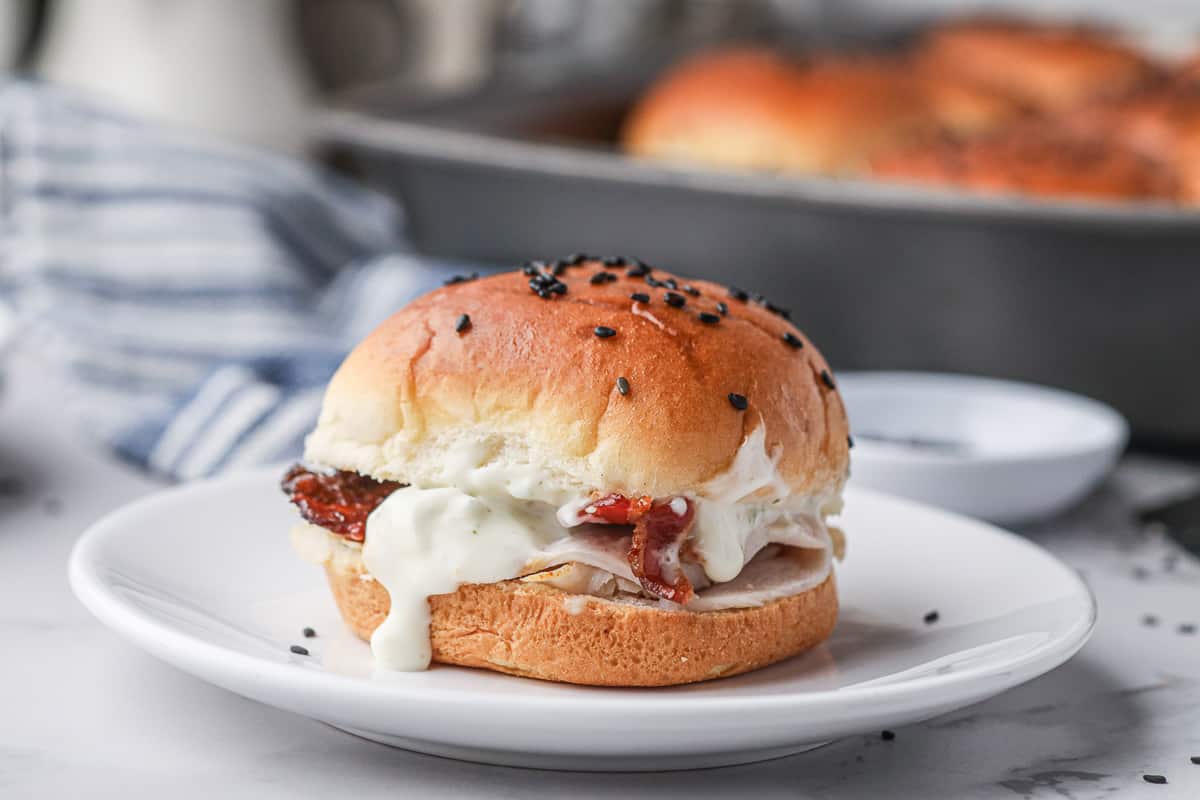 A close up of a slider with Ranch dressing oozing out from the middle on a white plate.