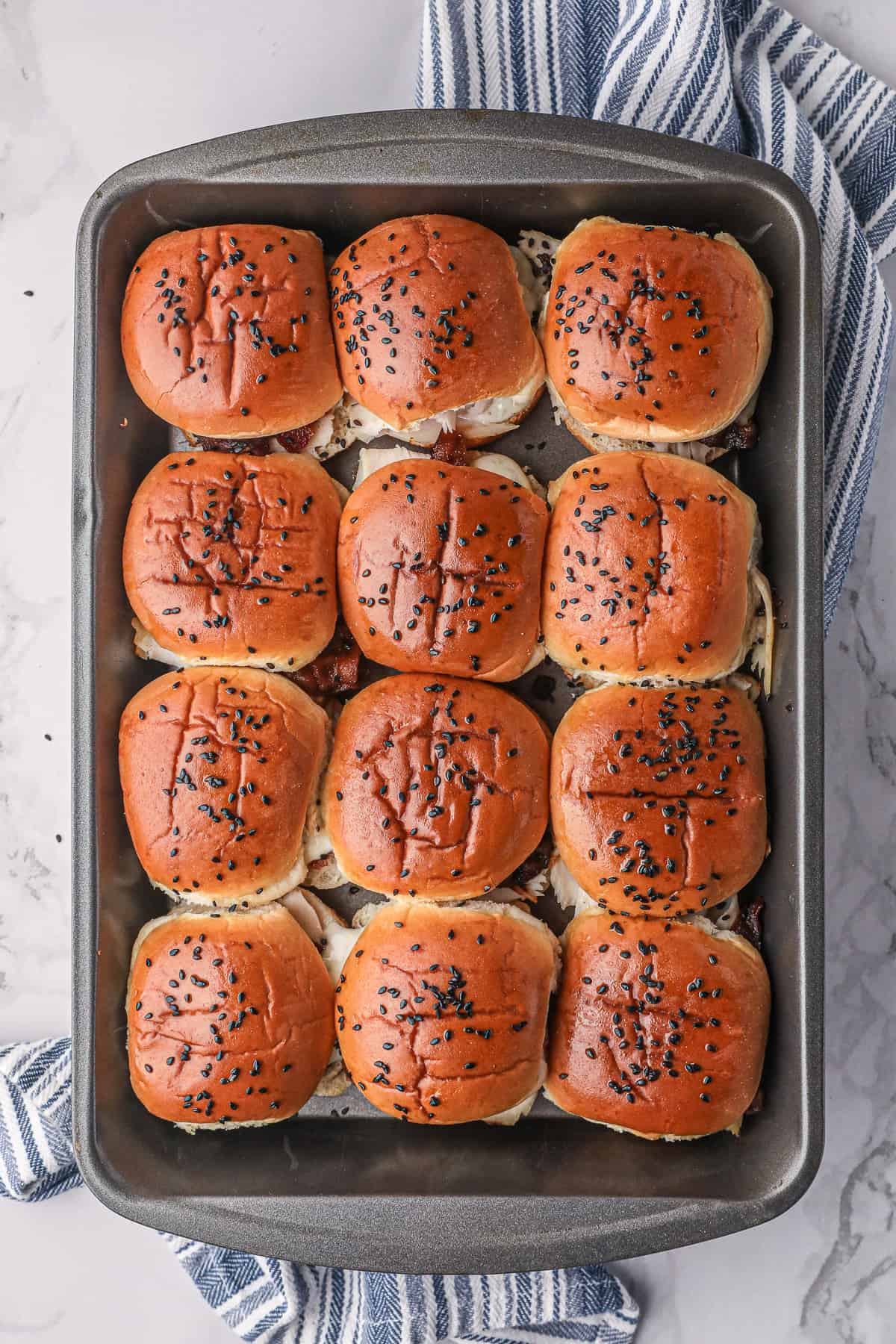 A top down shot of sliders in a metal pan on top of a blue and white kitchen towel.