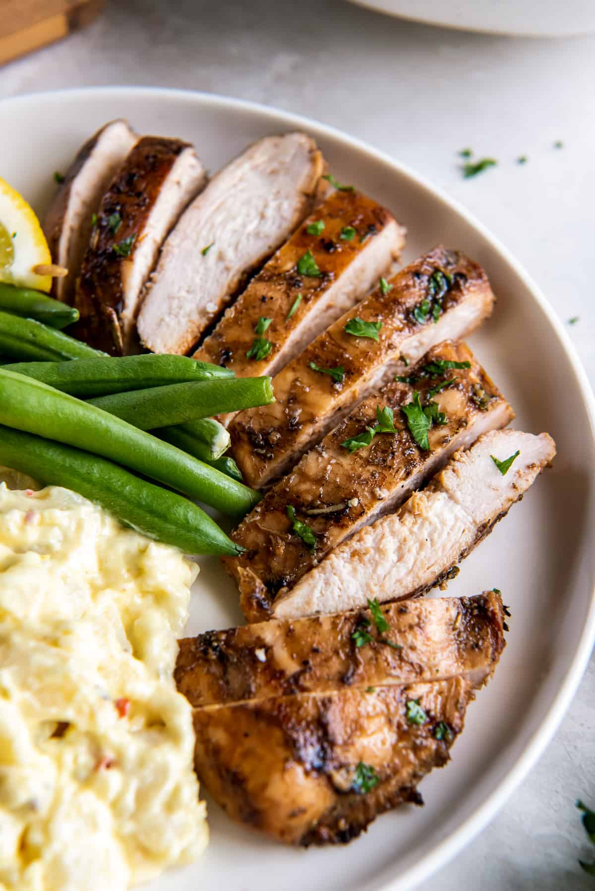 A sliced grilled chicken breast on a plate with potato salad and green beans.