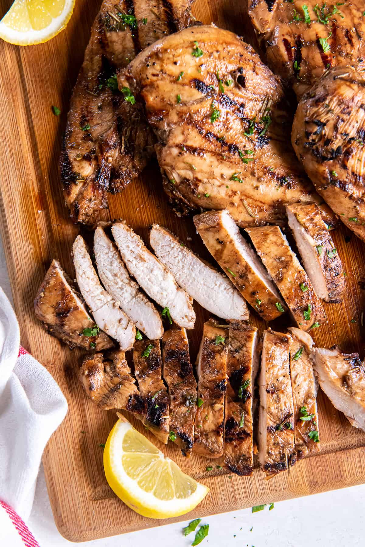 Sliced chicken on a cutting board with lemon wedges.