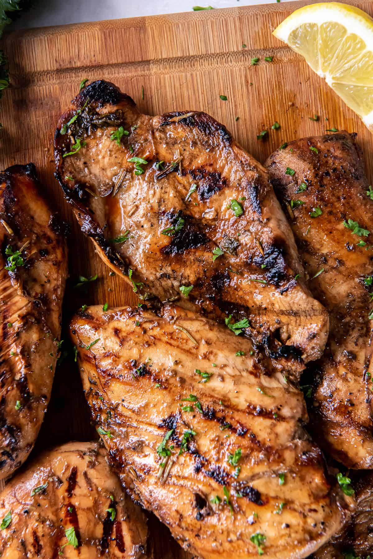 A top down shot of grilled chicken breasts on a cutting board with a lemon wedge.
