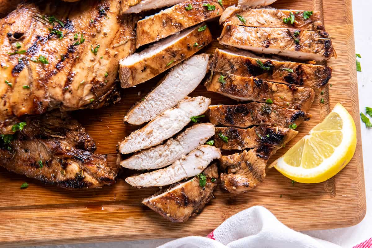 Sliced chicken on a cutting board with lemon wedges.