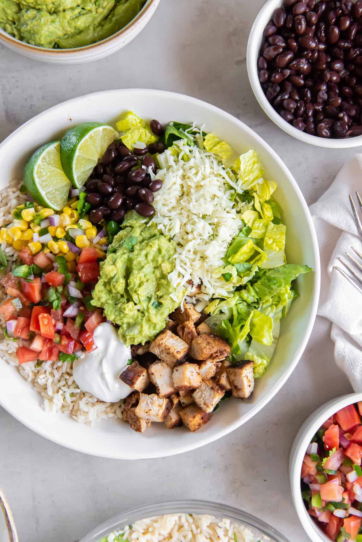 A top down shot of a copycat Chipotle burrito bowl with chicken next to small bowls filled with ingredients.