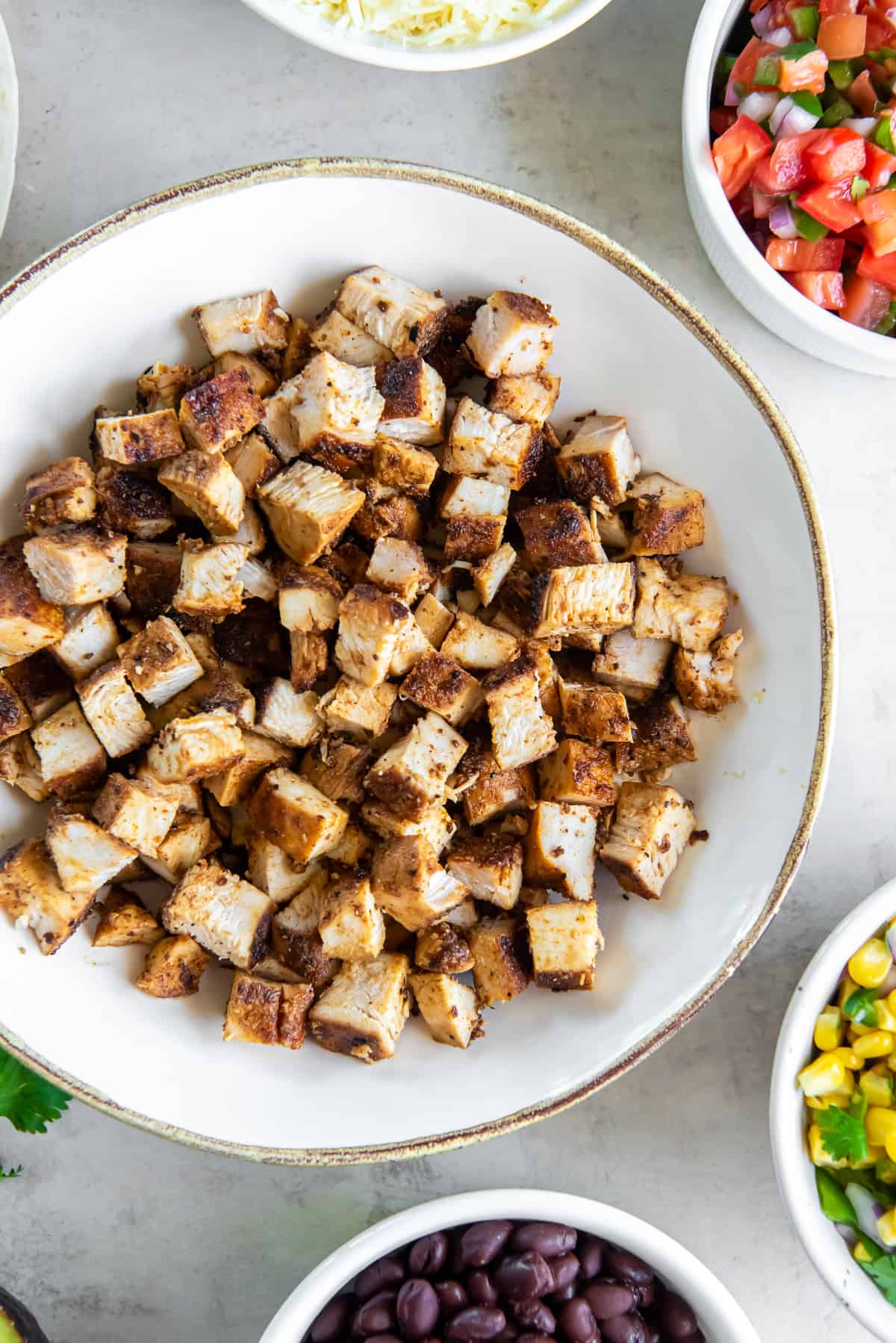 A top down shot of copycat Chipotle chicken in a white bowl surrounded by other ingredients in bowls.