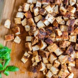 A top down shot of cooked, cubed chicken on a cutting board with cilantro sprigs.