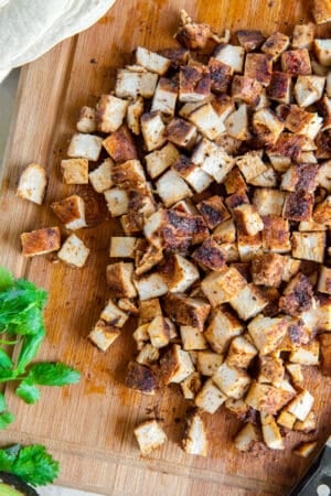 A top down shot of cooked, cubed chicken on a cutting board with cilantro sprigs.