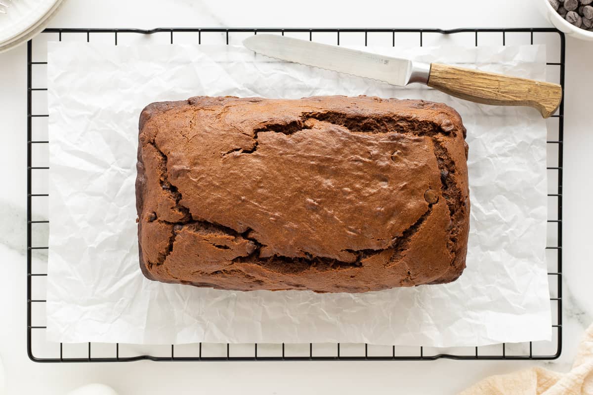 A top down shot of a loaf of chocolate peanut butter banana bread on a wire rack with a serrated knife.
