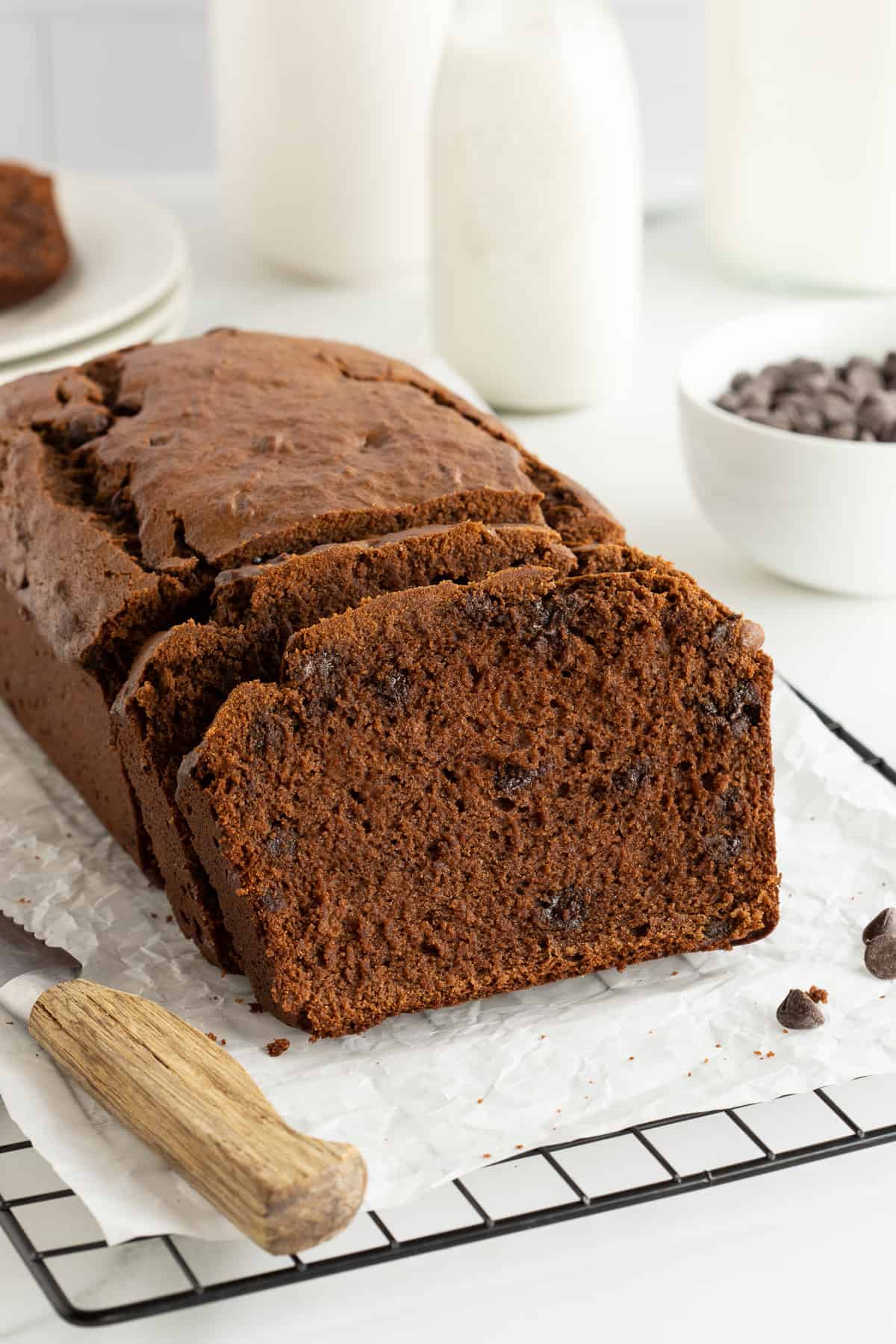 A side view of a sliced loaf of chocolate peanut butter banana bread on a wire rack with a serrated knife.