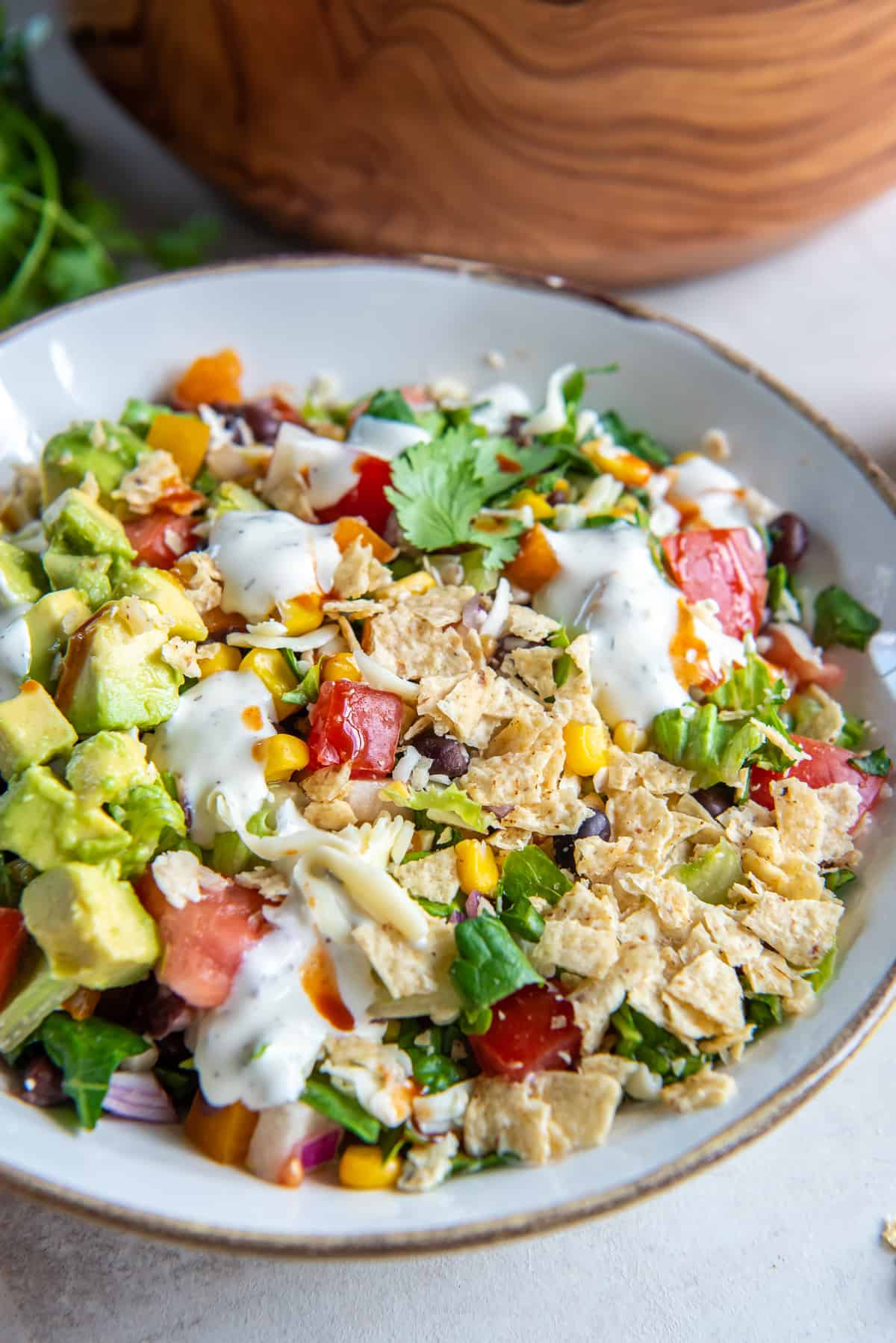 A bowl of southwest chopped salad topped with crushed tortilla chips and a drizzle of jalapeno ranch dressing.