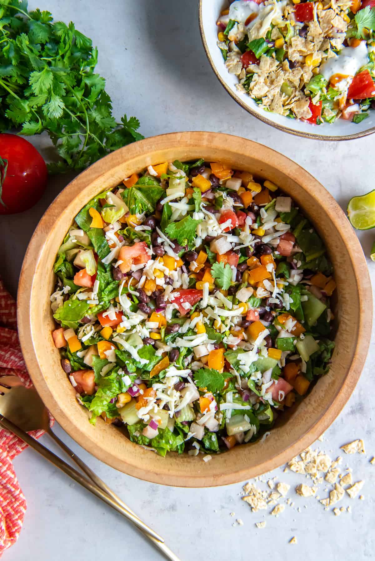 A top down shot of a chopped salad in a wood bowl next to a smaller bowl with serving of the salad and sprigs of cilantro.