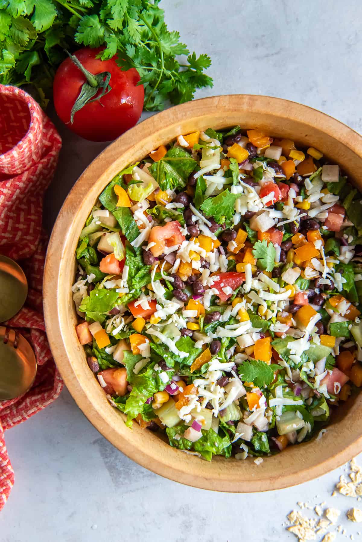 A top down shot of a chopped salad in a wood bowl next to a smaller bowl with serving of the salad and sprigs of cilantro.