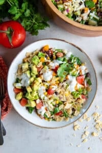 A top down shot of A bowl of southwest chopped salad topped with crushed tortilla chips and a drizzle of jalapeno ranch dressing.