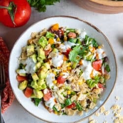 A top down shot of A bowl of southwest chopped salad topped with crushed tortilla chips and a drizzle of jalapeno ranch dressing.