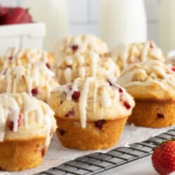 Glazed strawberry muffins on a wire rack on a kitchen counter.