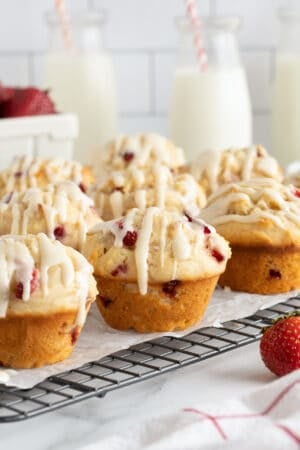 Glazed strawberry muffins on a wire rack on a kitchen counter.
