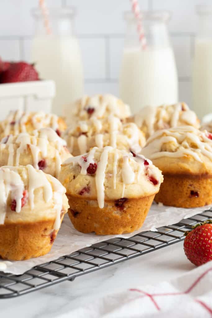 Glazed strawberry muffins on a wire rack on a kitchen counter.