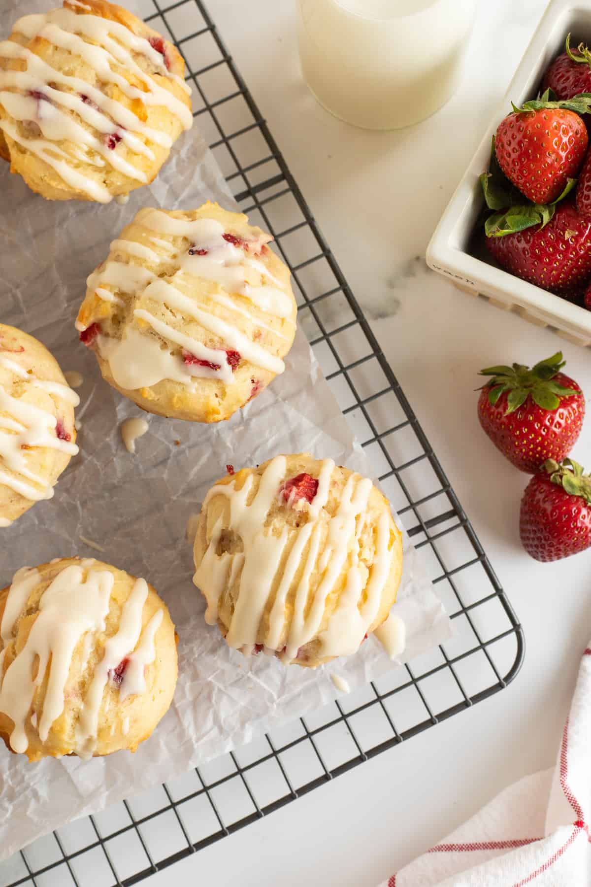 A top down shot of glazed strawberry muffins on a wire rack next to a container of fresh strawberries.