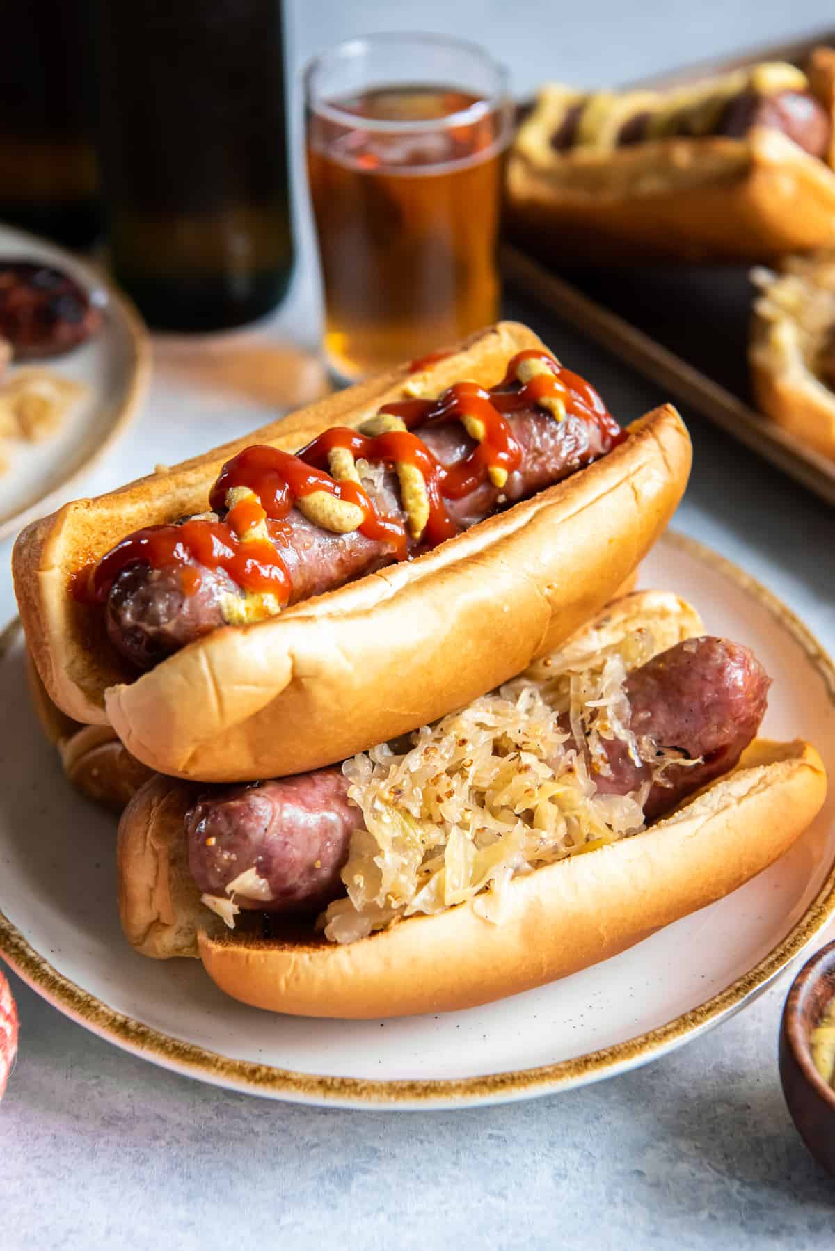 Bratwurst and sauerkraut in buns topped with ketchup stacked on top of each other on a plate.
