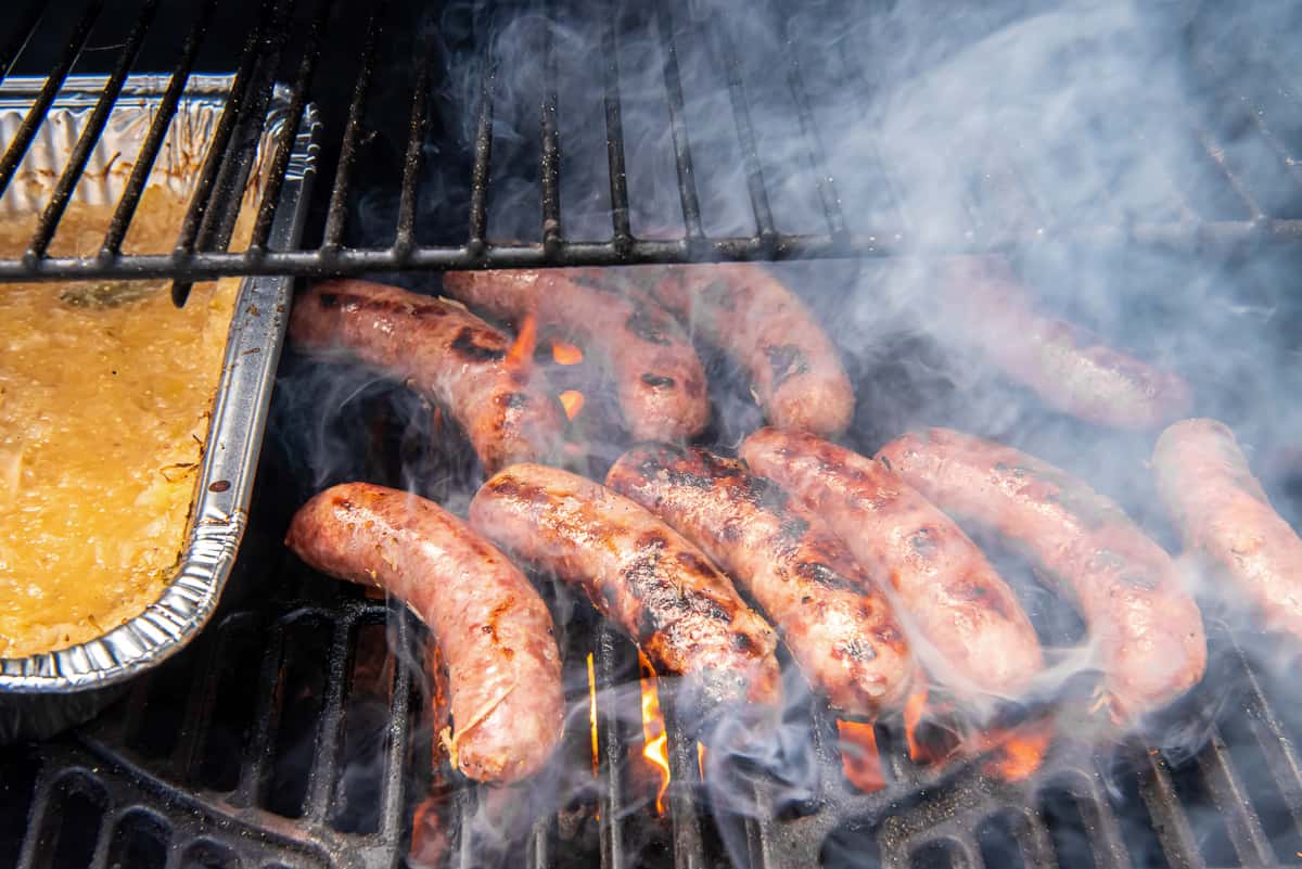 Bratwurst cooking on a gas grill grate.