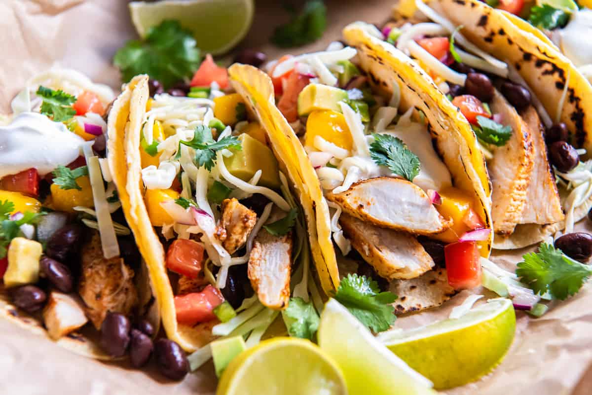 A side view of chicken tacos topped with mango salsa and cheese.