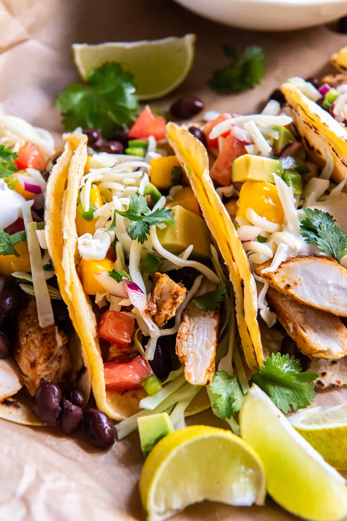 A side view of chicken tacos topped with mango salsa on parchment paper.