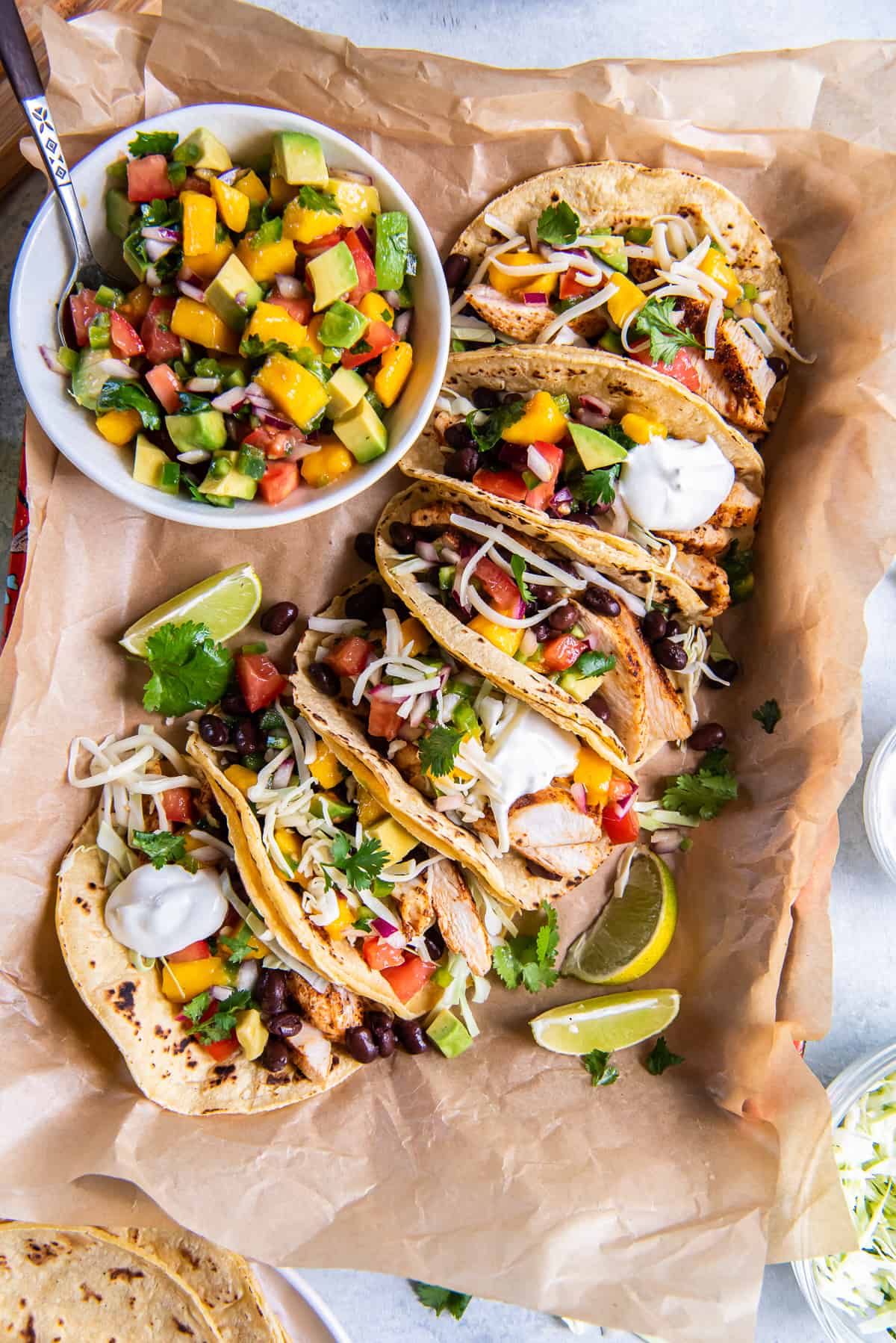 A top down shot of chicken tacos with mango salsa on parchment paper.