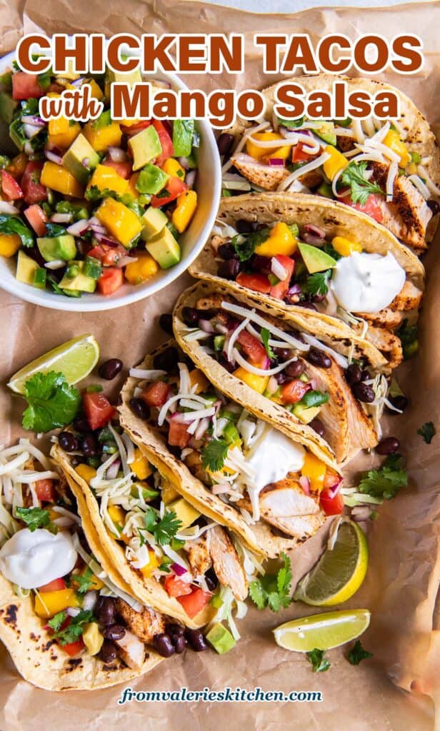 A top down shot of chicken tacos with mango salsa on parchment paper with text.
