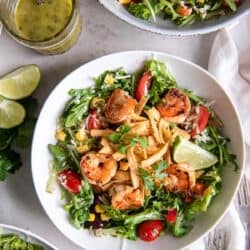 A top down shot of two bowls of Cilantro Lime Shrimp Salad next to a mason jar full of vinaigrette and lime wedges.