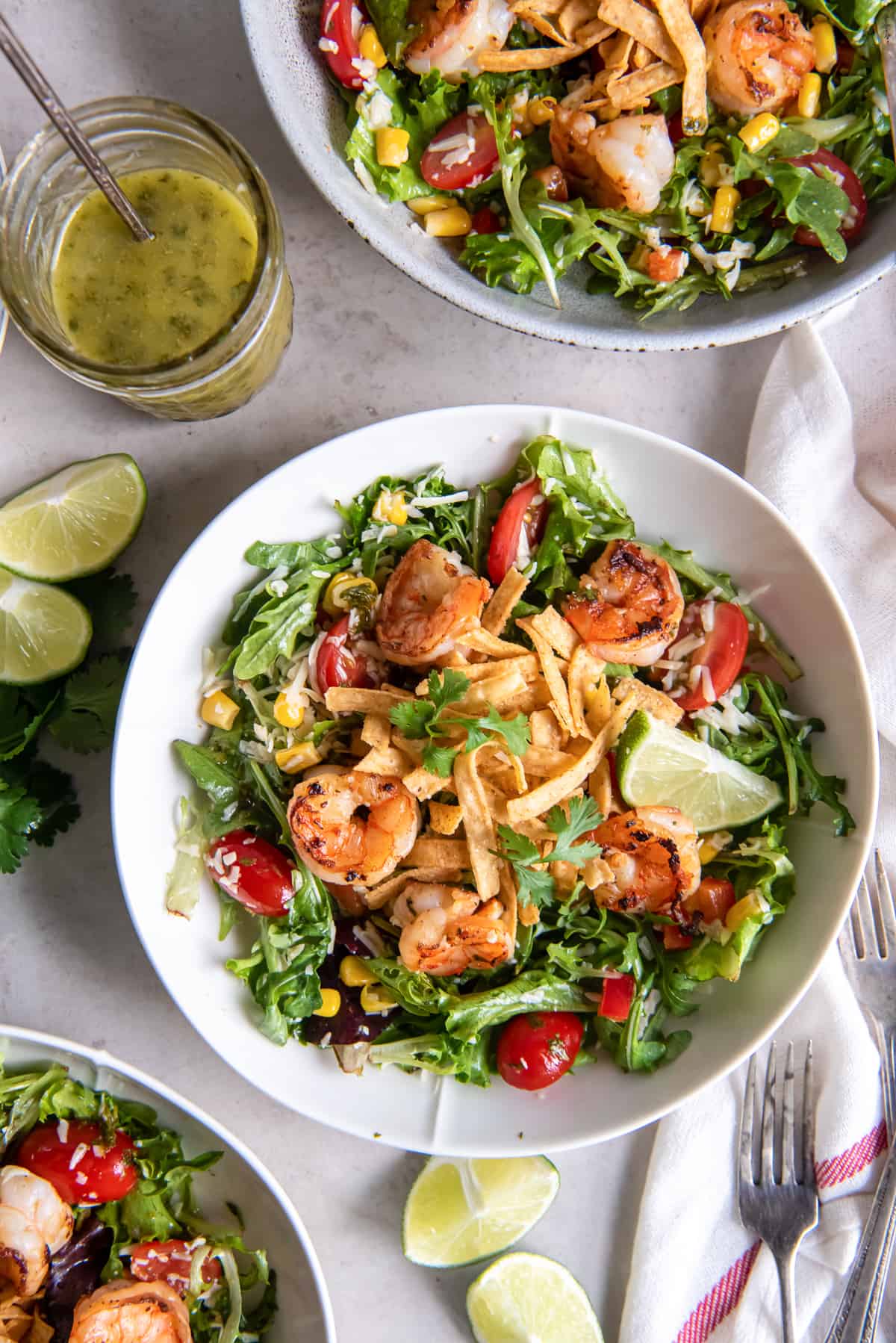 A top down shot of two bowls of Cilantro Lime Shrimp Salad next to a mason jar full of vinaigrette and lime wedges.